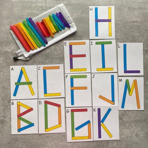 May include: A set of alphabet letter cards with colorful popsicle sticks arranged to form each letter. The letters are A, B, C, D, E, F, G, H, I, J, K, L, M.