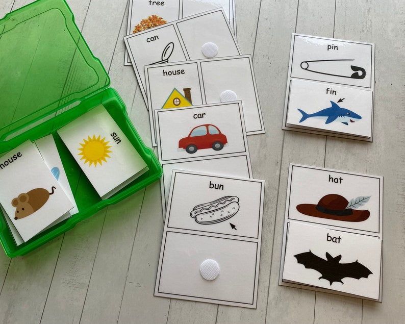 May include: A set of 10 flash cards with images and words for early learners. The cards feature a variety of objects, including a tree, can, house, car, sun, mouse, bun, hat, fin, and pin. The cards are designed to help children learn new words and concepts.