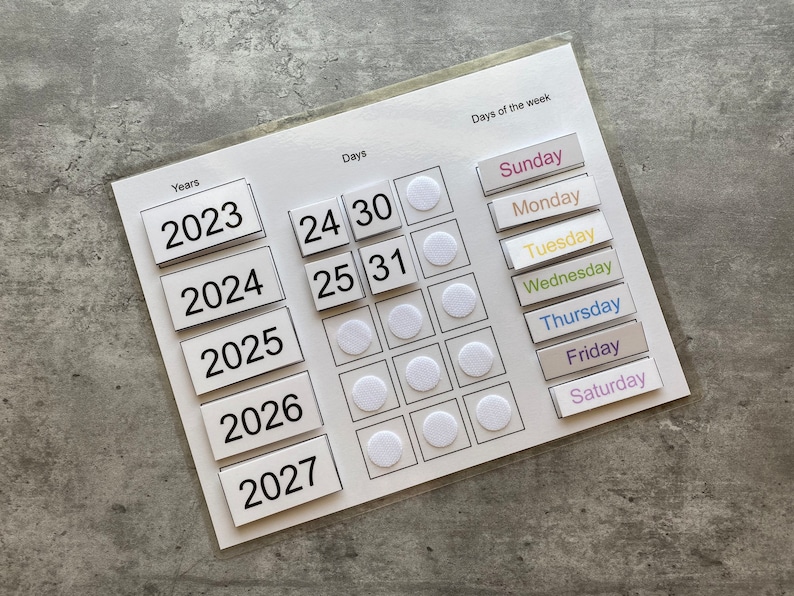 Pu&ograve; includere: Bacheca di calendario bianca con numeri neri e cerchi bianchi. La bacheca ha una sezione per gli anni, i giorni e i giorni della settimana. Gli anni sono 2023, 2024, 2025, 2026 e 2027. I giorni sono 24, 25, 30 e 31. I giorni della settimana sono domenica, luned&igrave;, marted&igrave;, mercoled&igrave;, gioved&igrave;, venerd&igrave; e sabato.
