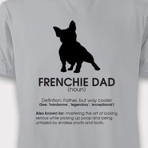 K&ouml;nnte beinhalten: Ein graues T-Shirt mit einer schwarzen Silhouette eines franz&ouml;sischen Bulldoggen und dem Text "FRENCHIE DAD (Substantiv)". Der Text unter der Silhouette definiert einen Frenchie Dad als einen Vater, der cool, gutaussehend, legend&auml;r und au&szlig;ergew&ouml;hnlich ist. Der Text erw&auml;hnt auch, dass ein Frenchie Dad daf&uuml;r bekannt ist, die Kunst zu beherrschen, ernst zu wirken, w&auml;hrend er Kot aufsammelt und von endlosen Schn&uuml;ffeln und Furzen unbeeindruckt bleibt.