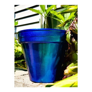 May include: A blue iridescent ceramic planter with a textured finish. The planter is sitting on a stone surface.
