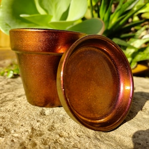 May include: A terracotta flower pot with a metallic copper and iridescent finish. The pot has a matching saucer.