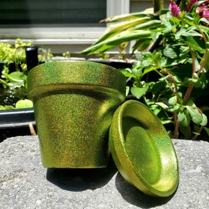 May include: A green glitter planter pot with a matching saucer. The pot and saucer are both made of ceramic and have a shiny, iridescent finish.