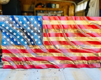 May include: A wooden American flag with a red, white, and blue color scheme. The flag is carved to look like it is waving in the wind. The wood grain is visible in the flag.