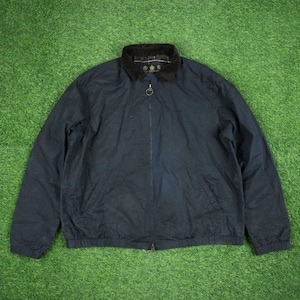 May include: A navy blue jacket with a black corduroy collar and a full-length zipper. The jacket has a ribbed hem and cuffs. The jacket is lying on a green surface.