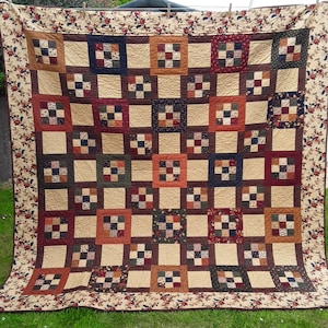 May include: A large patchwork quilt with a variety of squares in different colours and patterns, including brown, beige, red and green. The quilt is made up of smaller squares sewn together to create a larger design.