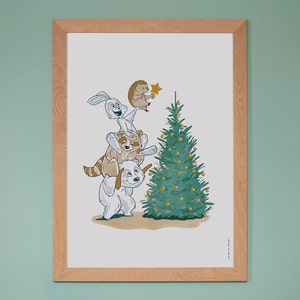 Könnte beinhalten: Ein gerahmter Druck mit einer skurrilen Weihnachtsillustration. Eine Ansammlung von Zeichentieren, darunter ein Hund, ein Waschbär und ein Hase, versammeln sich um einen geschmückten Weihnachtsbaum. Ein Igel setzt einen Stern auf. Der Rahmen ist aus hellem Holz.
