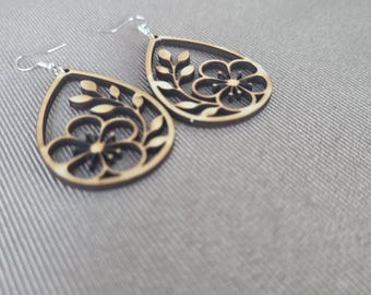 May include: A pair of teardrop-shaped wooden earrings featuring a laser-cut floral design with a central flower and surrounding leaves. The earrings are attached to silver-toned metal fishhook wires for pierced ears.