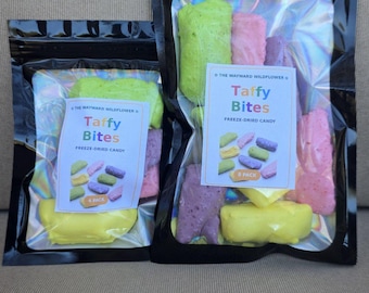 May include: Two black resealable pouches containing freeze-dried candy. Each bag features a label reading The Wayward Wildflower Taffy Bites Freeze-Dried Candy. The smaller bag is labeled 4 Pack, and the larger bag is labeled 8 Pack, showing colorful yellow, green, pink, and purple candy pieces.