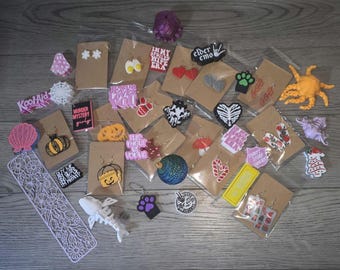 May include: A collection of assorted small plastic charms, earrings, and decorative items on brown cardstock backings. Items include miniature food, holiday symbols, text-based signs, animal shapes, and a white articulated skeleton figure.