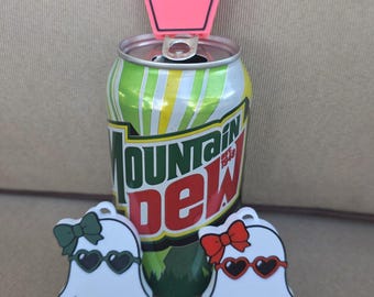 May include: A pink coffin-shaped tag with the black text BUT DID YOU DIE attached to a Mountain Dew soda can, flanked by two white ghost-shaped charms, one with a green bow and heart sunglasses, the other with a red bow and heart sunglasses.