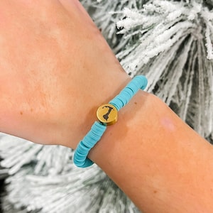 May include: A turquoise blue beaded bracelet with a gold charm featuring a silhouette of a state.