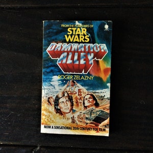 May include: A paperback book cover with a colorful illustration of a futuristic cityscape and a group of people. The title of the book is "Damnation Alley" and the author is Roger Zelazny. The cover also includes the text "From the publishers of Star Wars" and "Now a sensational 20th Century-Fox film."