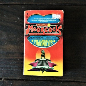 May include: A red, orange, and yellow paperback book cover with the title "The Cornelius Chronicles" by Michael Moorcock. The cover features a futuristic car with a person standing on top of it.