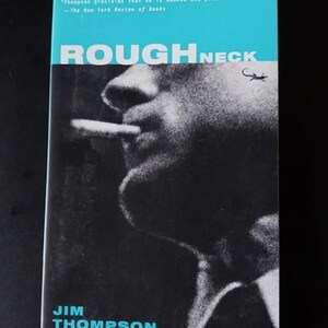 May include: A book cover with a black and white photo of a man smoking a cigarette. The title of the book is "ROUGHNECK" in white letters on a blue background. The author's name, "JIM THOMPSON", is in white letters on a blue background at the bottom of the cover.