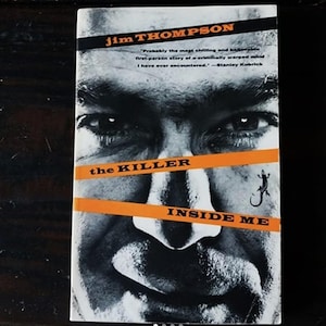 Può includere: Una fotografia in bianco e nero di un viso maschile sulla copertina di un libro tascabile. Il libro è intitolato "The Killer Inside Me" di Jim Thompson. Una citazione di Stanley Kubrick è stampata sulla copertina.