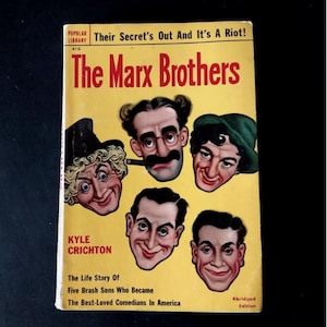 Peut inclure: Livre de poche vintage intitulé "The Marx Brothers" avec une couverture jaune. La couverture présente des illustrations des visages des Marx Brothers. Le livre comprend le texte "Their Secret's Out And It's A Riot!" et "The Life Story Of Five Brash Sons Who Became The Best-Loved Comedians In America."