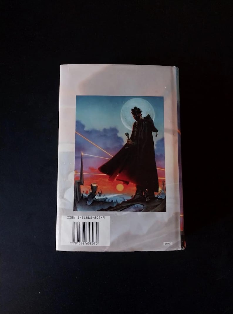Puede incluir: Contraportada de un libro con una ilustraci&oacute;n de fantas&iacute;a. Una figura con una capa oscura sostiene una espada contra un cielo iluminado por la luna y una puesta de sol ardiente. El ISBN y el c&oacute;digo de barras son visibles.