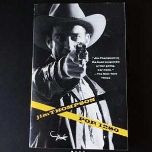 Può includere: Una fotografia in bianco e nero di un uomo con un cappello da cowboy che tiene una pistola. La copertina del libro presenta il testo "Jim Thompson" in strisce gialle e nere e "POP. 1280" in giallo. La citazione "Jim Thompson è il miglior scrittore di suspense in circolazione, senza dubbio." - The New York Times è stampata sulla copertina.