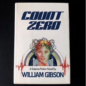 May include: A vintage paperback book titled "Count Zero" by William Gibson. The cover features a futuristic illustration of a person's face with colorful wiring and a red and white heartbeat-like design.
