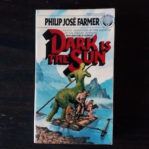 May include: A paperback book cover with a blue, green, and brown illustration of a creature with a human torso and a reptilian tail, riding a raft with other figures. The title of the book is "Dark is the Sun" by Philip José Farmer.
