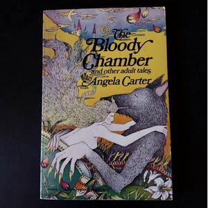 May include: A vintage paperback book titled "The Bloody Chamber and other adult tales" by Angela Carter. The cover features a yellow background with an illustration of a woman embracing a wolf. The artwork includes a castle, moon, and floral elements.