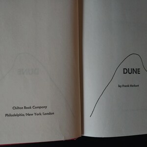 以下が含まれることがあります： 開いた本のページで、フランク・ハーバート著「DUNE」のタイトルが表示されています。本の表紙には山のようなイラストが描かれています。出版社名Chilton Book Companyと、都市名フィラデルフィア、ニューヨーク、ロンドンも表示されています。