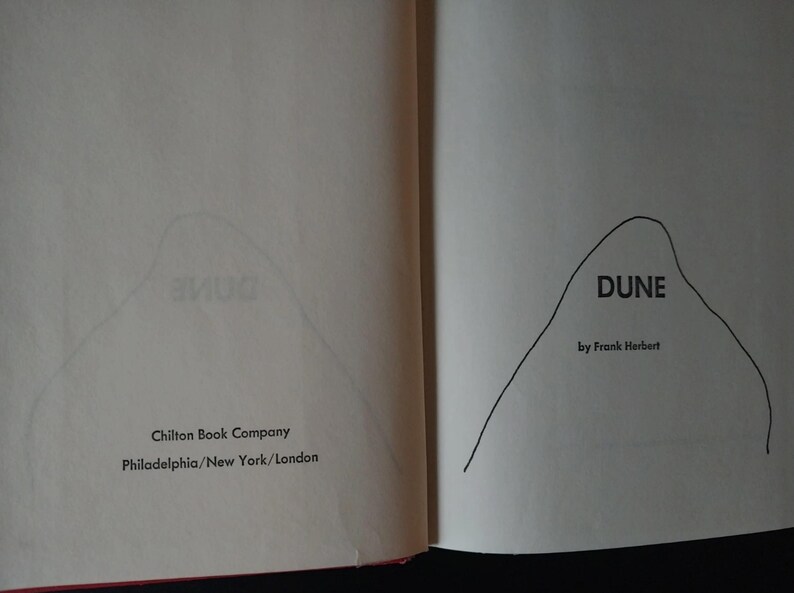 以下が含まれることがあります： 開いた本のページで、フランク・ハーバート著「DUNE」のタイトルが表示されています。本の表紙には山のようなイラストが描かれています。出版社名Chilton Book Companyと、都市名フィラデルフィア、ニューヨーク、ロンドンも表示されています。