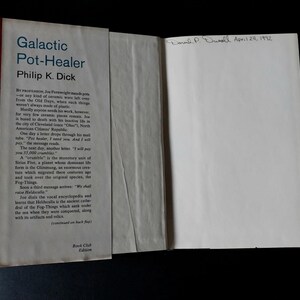 以下が含まれることがあります： フィリップ・K・ディック著「Galactic Pot-Healer」というタイトルの開かれた本。表紙は明るい色で黒い文字が書かれています。この本はブッククラブ版です。内側のページには手書きで「Donald P. Chinell April 24, 1992」と書かれています。