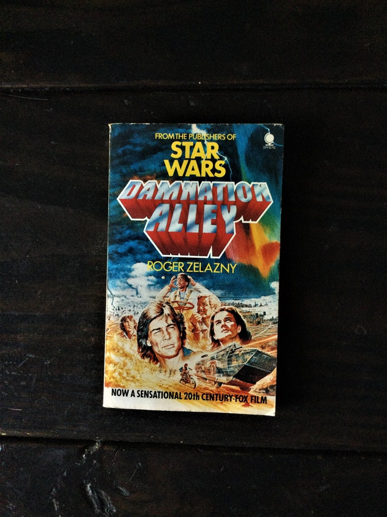 May include: A paperback book cover with a colorful illustration of a futuristic cityscape and a group of people. The title of the book is "Damnation Alley" and the author is Roger Zelazny. The cover also includes the text "From the publishers of Star Wars" and "Now a sensational 20th Century-Fox film."
