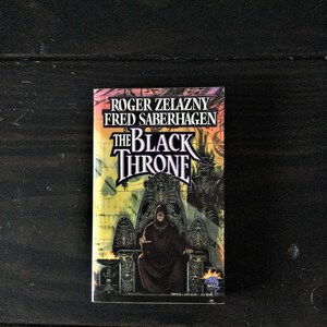 May include: A paperback book cover with a black and white illustration of a person sitting on a throne. The title of the book is "The Black Throne" and the authors are Roger Zelazny and Fred Saberhagen.