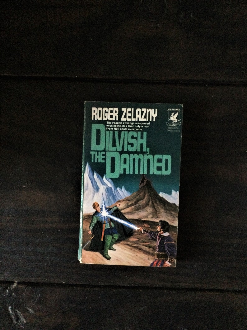 May include: A paperback book cover with a green and white design. The title is "Dilvish, The Damned" by Roger Zelazny. The cover features a man in green armor holding a sword and a man in black armor holding a sword. The background is a snowy mountain range.
