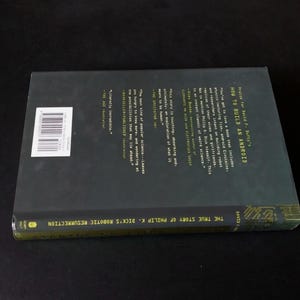 以下が含まれることがあります： デビッド・F・ダフティ著の「How to Build an Android」というタイトルのハードカバー本。本は、白い文字とバーコードステッカーが付いた濃い緑色の表紙です。本の背表紙には「The True Story of Philip K. Dick's Robotic Resurrection」と書かれています。
