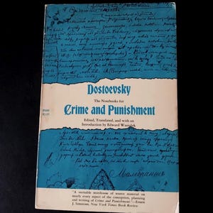 May include: A vintage paperback book titled "Crime and Punishment" by Dostoevsky. The cover features blue and white hues with handwritten script and the author's name. The book is a literary classic.