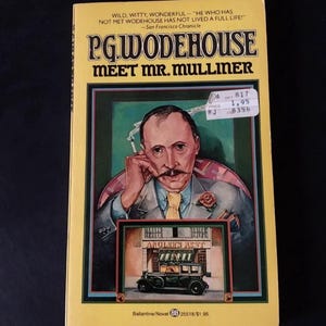 May include: A paperback book titled Meet Mr. Mulliner by P.G. Wodehouse with a yellow cover. The cover features an illustration of a man with a mustache holding a cigarette, and a smaller image of a vintage car parked in front of the Angler's Rest.