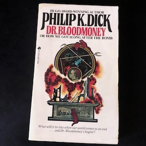 Peut inclure: Un livre de poche vintage intitulé "Dr. Bloodmoney" de Philip K. Dick. La couverture présente une illustration surréaliste avec un design circulaire, des personnages et un fond enflammé. Le titre et l'auteur sont mis en évidence.