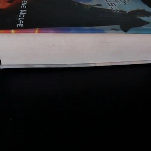 Puede incluir: Un libro de tapa dura con una cubierta colorida y p&aacute;ginas blancas. El t&iacute;tulo del libro y el nombre del autor son visibles en la cubierta. El libro est&aacute; sobre un fondo negro.