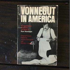 May include: A black and white photo of Kurt Vonnegut on the cover of a book titled "Vonnegut in America". The book cover also includes the text "An Introduction to the Life and Work of Kurt Vonnegut" and "Original Essays Edited by Jerome Klinkowitz and Donald L. Lawler".