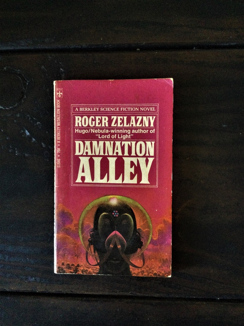 May include: A red paperback book with the title "Damnation Alley" by Roger Zelazny. The book cover features a futuristic illustration of a person wearing a helmet and a dark background.