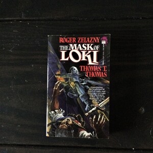 May include: A paperback book cover with a dark blue background and a colorful illustration of a person falling. The title of the book is "The Mask of Loki" by Roger Zelazny and Thomas T. Thomas.