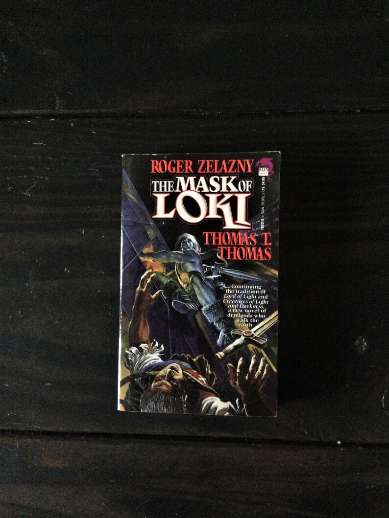 May include: A paperback book cover with a dark blue background and a colorful illustration of a person falling. The title of the book is "The Mask of Loki" by Roger Zelazny and Thomas T. Thomas.