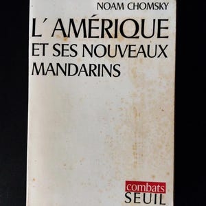 Può includere: Copertina di un libro con il titolo "L'AMÉRIQUE ET SES NOUVEAUX MANDARINS" di Noam Chomsky. La copertina è bianco sporco con testo nero e un logo rosso che dice "combats SEUIL". Il libro è leggermente usurato.