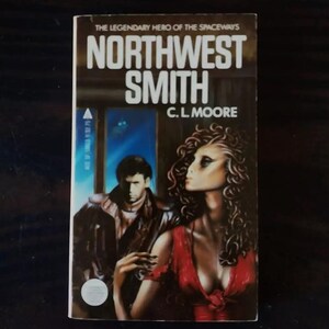 Op de afbeelding: Een paperback boekomslag met een donkere achtergrond en een kleurrijke illustratie van een vrouw met lang, donker haar en een man met kort, donker haar. De titel van het boek is "Northwest Smith" en de auteur is "C.L. Moore".