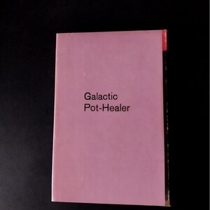 以下が含まれることがあります： 黒い背景に、タイトル「Galactic Pot-Healer」と書かれたピンク色の本。本の右上には赤いタブが付いています。テキストはシンプルなサンセリフ体です。