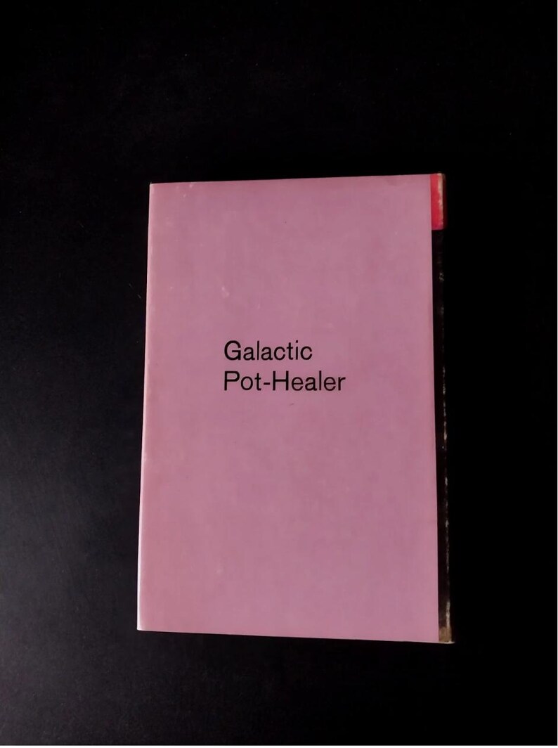 以下が含まれることがあります： 黒い背景に、タイトル「Galactic Pot-Healer」と書かれたピンク色の本。本の右上には赤いタブが付いています。テキストはシンプルなサンセリフ体です。