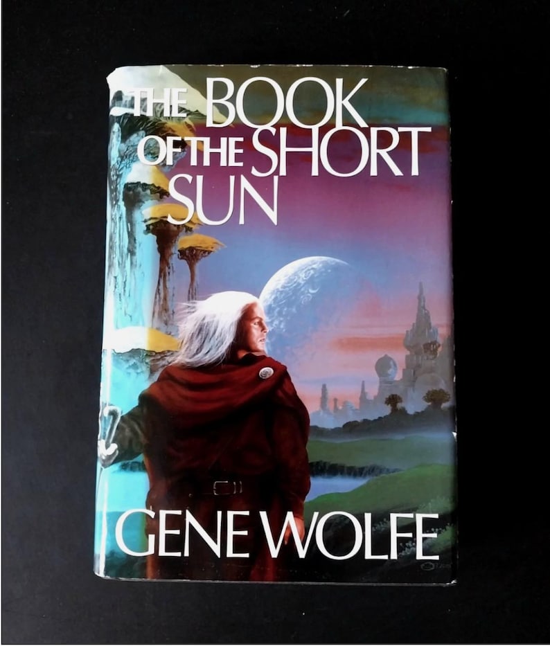 Puede incluir: Un libro de bolsillo vintage titulado "The Book of the Short Sun" de Gene Wolfe. La portada presenta a una persona con cabello blanco y una capa roja, sobre un fondo de un planeta y una ciudad futurista. El libro tiene un esquema de color azul y morado.