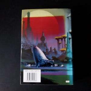Puede incluir: Contraportada de un libro de bolsillo con una ilustraci&oacute;n de ciencia ficci&oacute;n. La obra de arte representa una ciudad futurista bajo un cielo rojo, con una gran estructura blanca en forma de nave espacial. Una etiqueta blanca con c&oacute;digo de barras es visible.