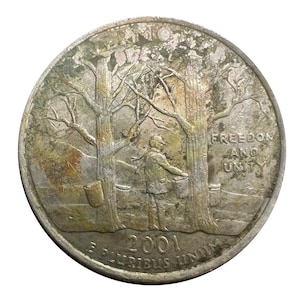May include: A silver quarter coin featuring a detailed depiction of a person collecting sap from trees in a forest. The coin is inscribed with "FREEDOM AND UNITY" and the year "2001". The coin also has the inscription "E PLURIBUS UNUM".