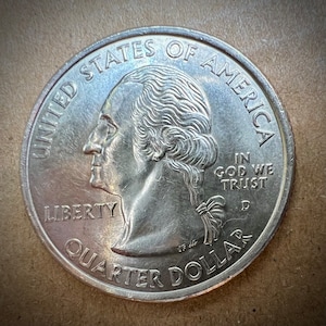 May include: A silver US quarter dollar coin with the profile of George Washington on the obverse. The coin reads "United States of America", "Liberty", "In God We Trust", and "Quarter Dollar".