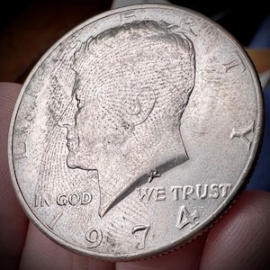 May include: A silver US half dollar coin with the profile of John F. Kennedy on the obverse. The coin has the inscription "IN GOD WE TRUST" and the date "1967".